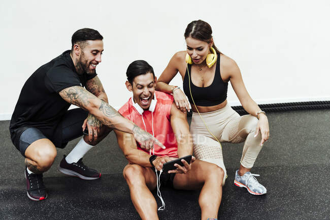 Sportler lacht bei Handy-Nutzung durch Freunde im Fitnessstudio — Stockfoto