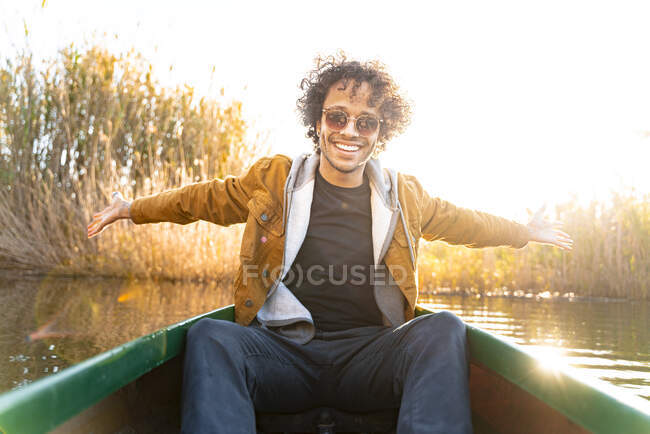 Smiling man sitting with arms outstretched in canoe on river — Stock Photo