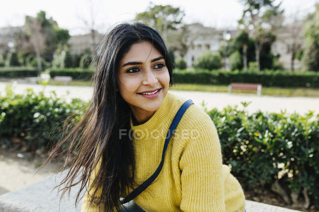 Donna sorridente in maglione guardando altrove mentre seduto nel parco — Foto stock