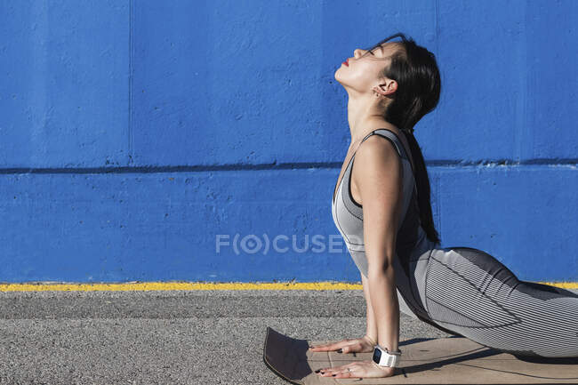 Woman doing Urdhva Mukha Svanasana by blue wall — Stock Photo
