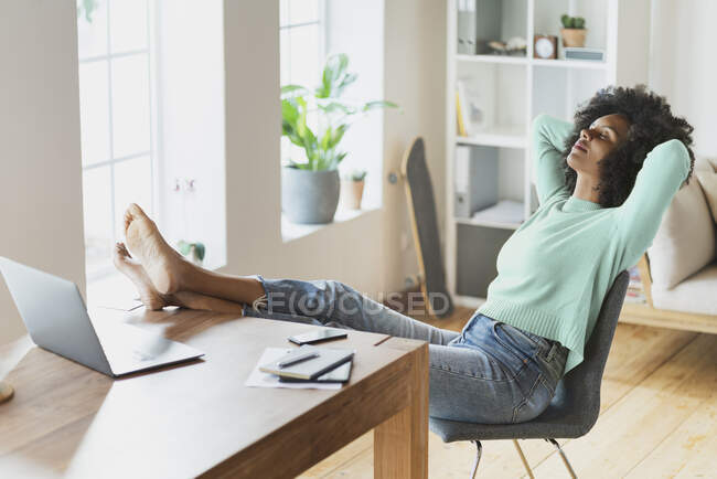 Woman with hands behind head relaxing on chair at home — Stock Photo