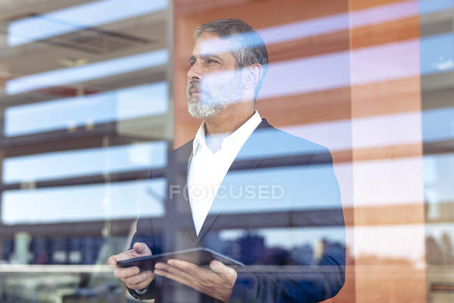 Задумчивый предприниматель с цифровым планшетом смотрит в сторону, стоя в современном офисе — стоковое фото