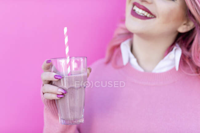 Mujer sonriente sosteniendo un vaso de batido frente a la pared - foto de stock