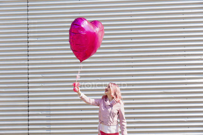 Mujer feliz mirando el globo en forma de corazón durante el día soleado - foto de stock