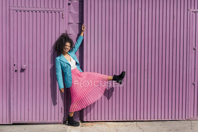 Усміхнена молода жінка під час танцю з пурпурової металевої стіни. — стокове фото