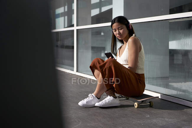 Asiatin nutzt Smartphone bei sonnigem Wetter auf Skateboard — Stockfoto