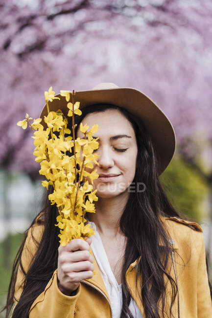 Mujer sonriente con los ojos cerrados sosteniendo flores amarillas durante la primavera - foto de stock