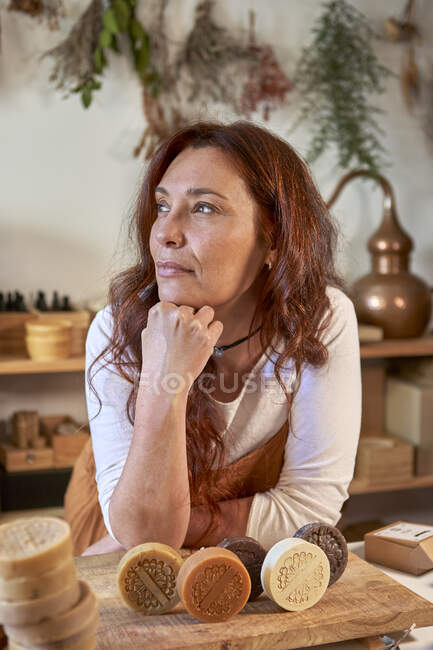 Mujer pensativa con jabones orgánicos sobre tabla de madera en el taller - foto de stock