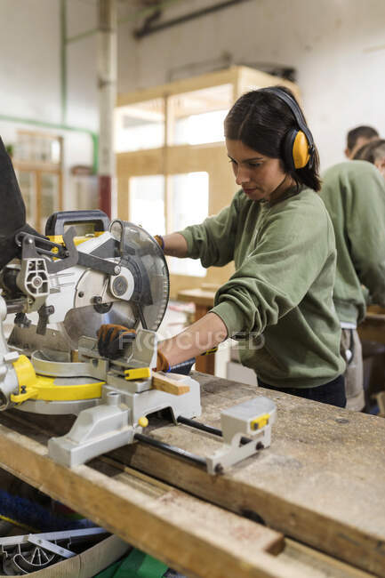 Carpintero femenino con orejera que utiliza equipo de carpintería en el banco de trabajo de la industria - foto de stock