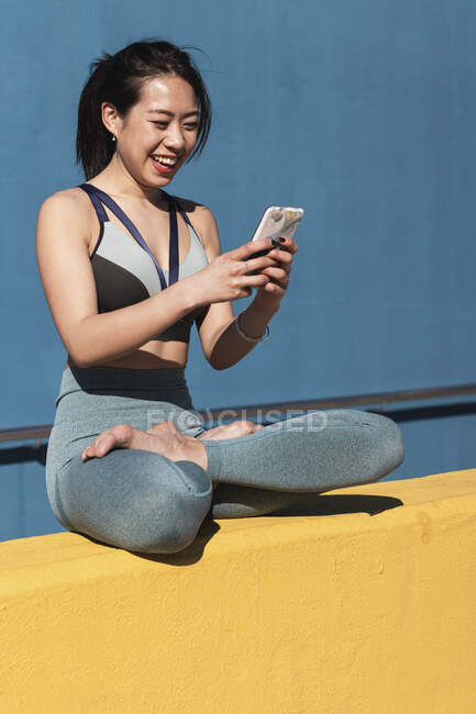 Happy beautiful woman using smart phone while sitting on retaining wall — Stock Photo