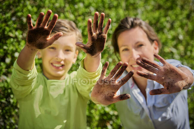 Madre con hijo mostrando las manos de barro en el jardín durante el día soleado - foto de stock