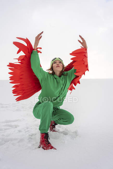 Femme avec les bras levés en position accroupie regardant la neige contre le ciel — Photo de stock