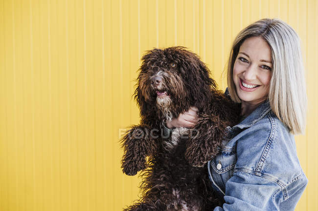 Mujer sonriente llevando perro por la pared amarilla - foto de stock