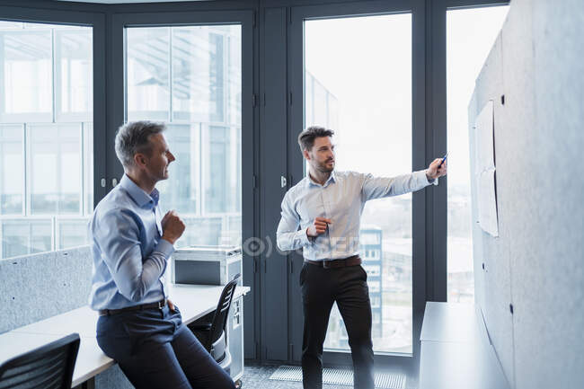 Geschäftsmann erklärt Papier über Pinnwand mit männlichem Amtskollegen — Stockfoto
