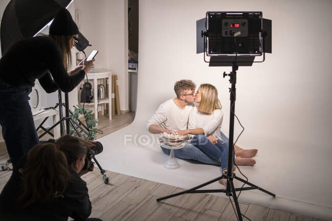 Casal com bolo beijando ao fazer sessão de fotos em estúdio — Fotografia de Stock