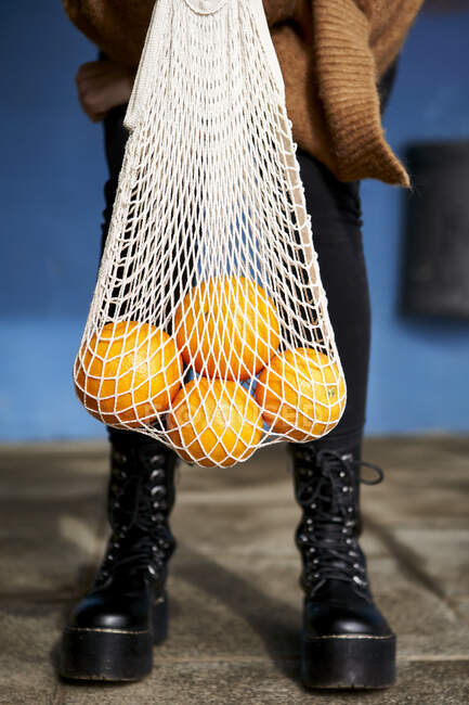 Giovane donna che tiene le arance in borsa riutilizzabile mentre in piedi sul sentiero — Foto stock