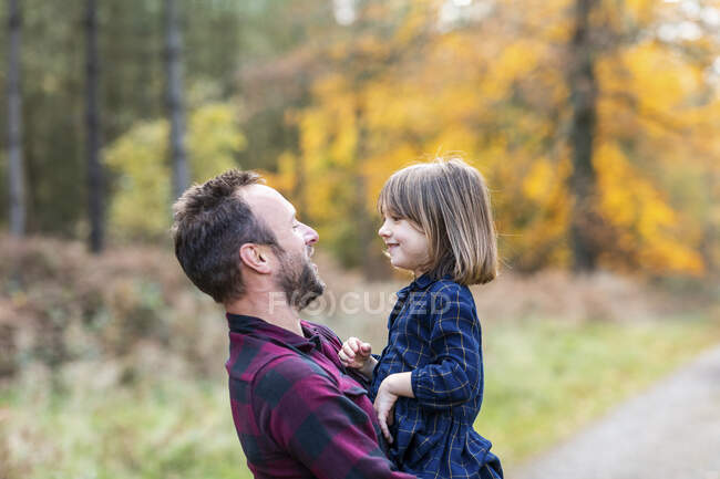 Padre llevando a su hija en brazos mientras está de pie en el bosque - foto de stock