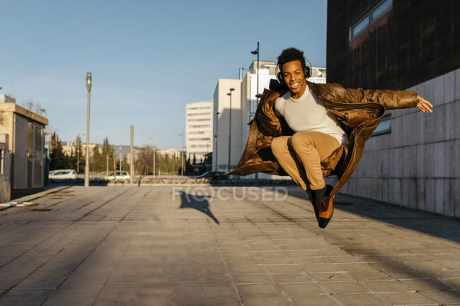 Homme souriant portant des écouteurs sautant tout en pratiquant la danse au coucher du soleil — Photo de stock