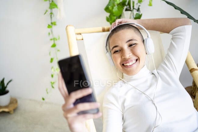 Giovane donna che utilizza smartphone durante l'ascolto di musica attraverso le cuffie a casa — Foto stock