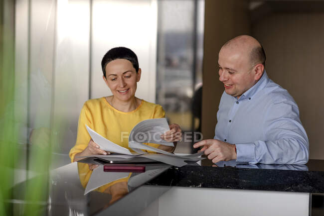 Lächelnde Geschäftsfrau liest Dokument, während sie mit männlichen Kollegen im modernen Büro diskutiert — Stockfoto