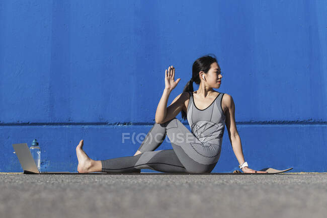 Donna che fa esercizio di stretching mentre seduto vicino al muro blu — Foto stock