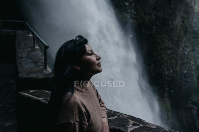 Woman contemplating while leaning on retaining wall by waterfall — Stock Photo