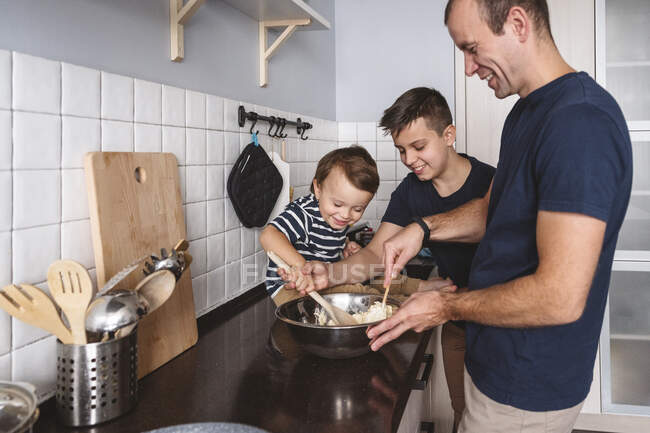 Cheerful sons helping father to prepare food in kitchen at home — Stock Photo