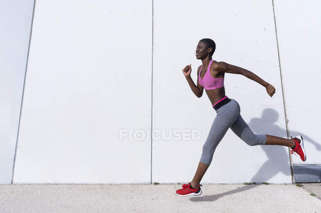 Atleta feminina sorrindo correndo contra a parede branca — Fotografia de Stock