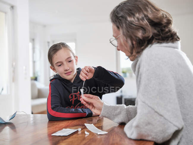 Chica con madre examinando covid-19 prueba en casa - foto de stock