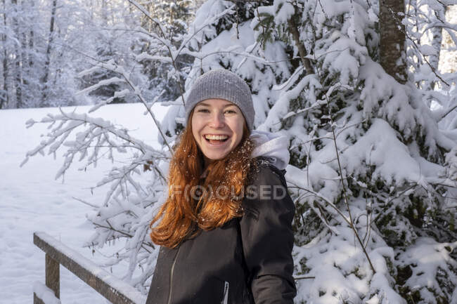 Счастливая женщина с рыжими волосами перед заснеженным деревом зимой — стоковое фото