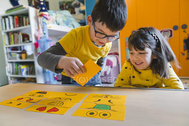 Niños juguetones con emoticonos en la mesa en la sala de juegos en casa - foto de stock
