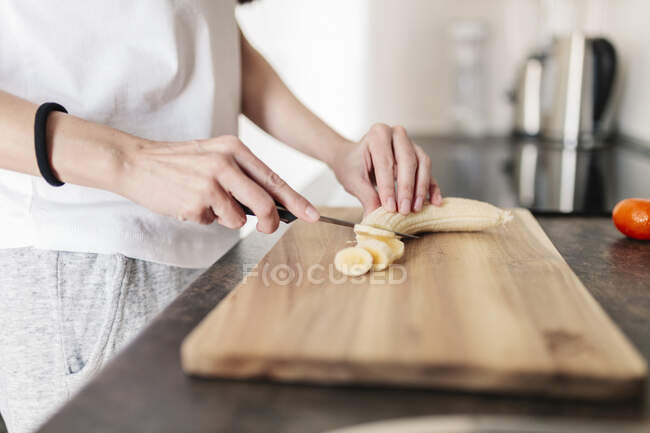 Mujer madura cortando plátano a bordo en la cocina - foto de stock