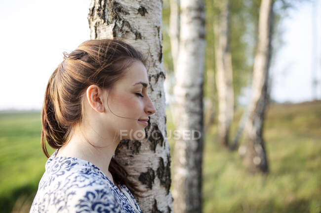 Giovane donna con gli occhi chiusi appoggiata su un tronco d'albero godendo della natura — Foto stock