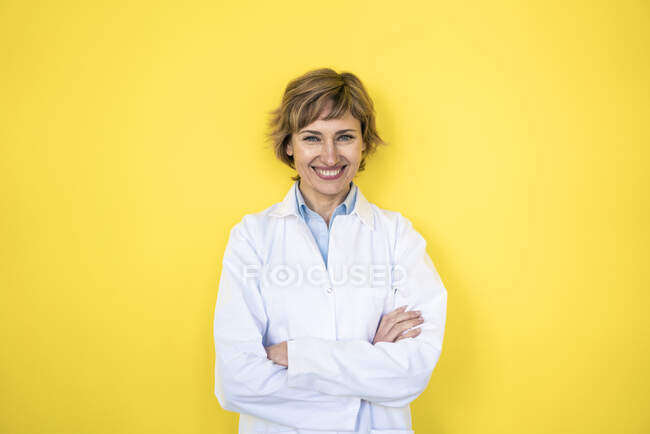 Científica sonriente de pie con los brazos cruzados frente a la pared - foto de stock