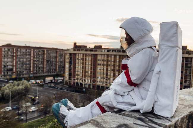 Молодая женщина-астронавт, сидящая на подпорной стене во время заката — стоковое фото