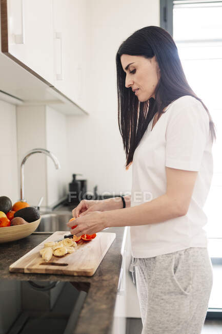 Mujer madura cortando plátano en la cocina - foto de stock