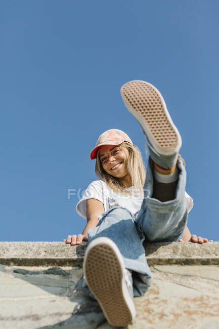 Femme souriante portant une casquette assise devant le ciel bleu — Photo de stock