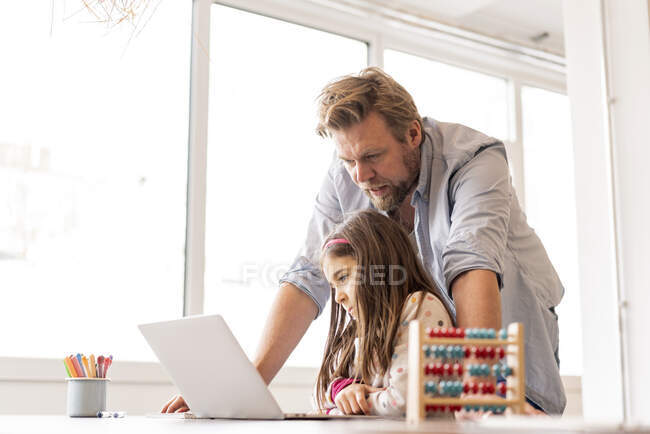 Девушка учится на ноутбуке с мужчиной, стоящим позади дома — стоковое фото