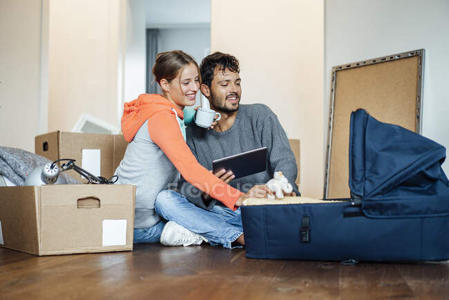 Jeune couple souriant assis avec porte-bébé à la nouvelle maison — Photo de stock