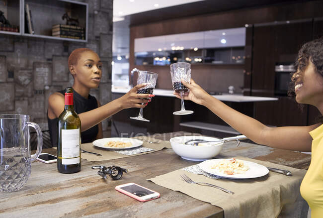 Deux amis dînent ensemble à la maison pour griller avec du vin rouge — Photo de stock