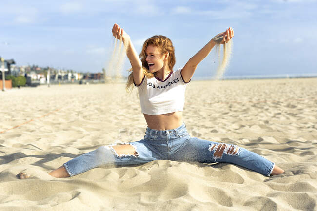 Беззаботная молодая женщина играет с песком на пляже в солнечный день — стоковое фото