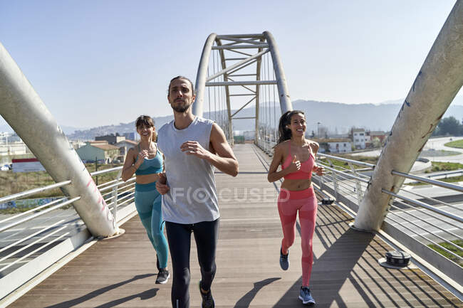 Multi ethnic health conscious friends running on bridge — Stock Photo
