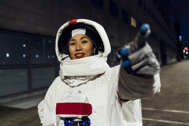 Smiling female astronaut in space suit pointing on footpath at night — Stock Photo