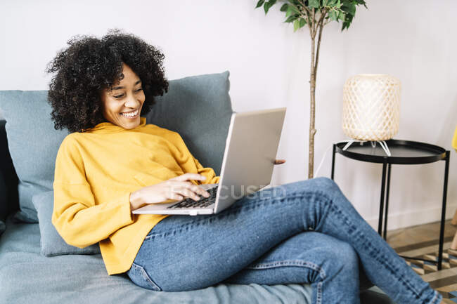 Smiling young woman using laptop while sitting on sofa at home — Stock Photo
