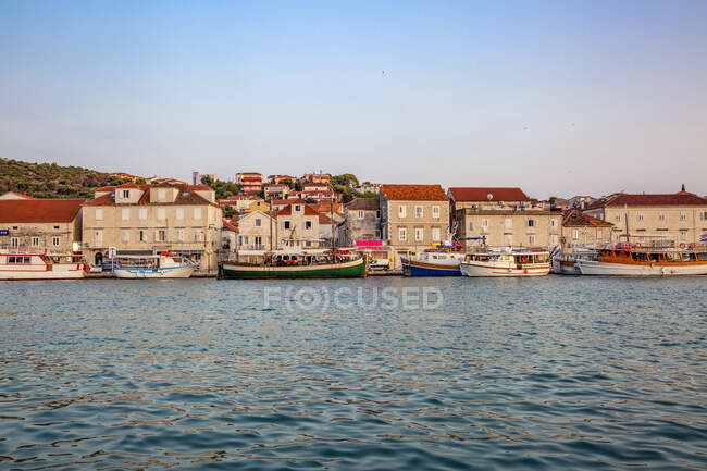 Хорватія, округ Спліт-Далмація, Трогір, човни пришвартовані вздовж узбережжя острова Чіово з будинками на задньому плані — стокове фото