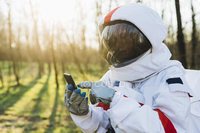 Young astronaut with space suit and helmet using smart phone in forest — Fotografia de Stock
