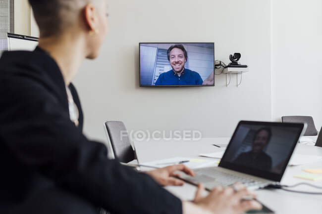 Businesswoman attending meeting with colleague through video call on laptop and television at office — Foto stock