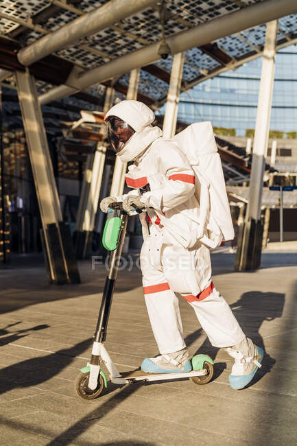 Male astronaut riding electric scooter in city — Stock Photo