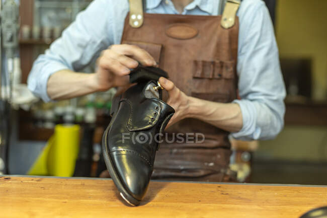 Male cobbler holding shoe while polishing at workshop — Stock Photo