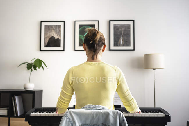 Mid adult woman learning piano in front of picture frame at home — Stock Photo